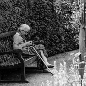 Alte Frau im Park mit Handy.